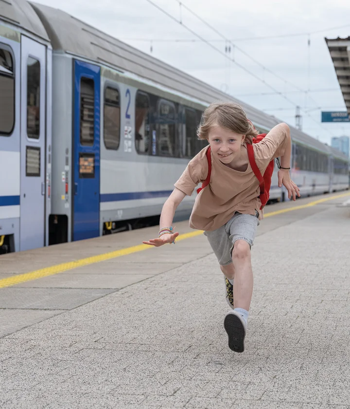 dziecko z czerwonym plecakiem biegnie wzdłuż pociągu na stacji kolejowej