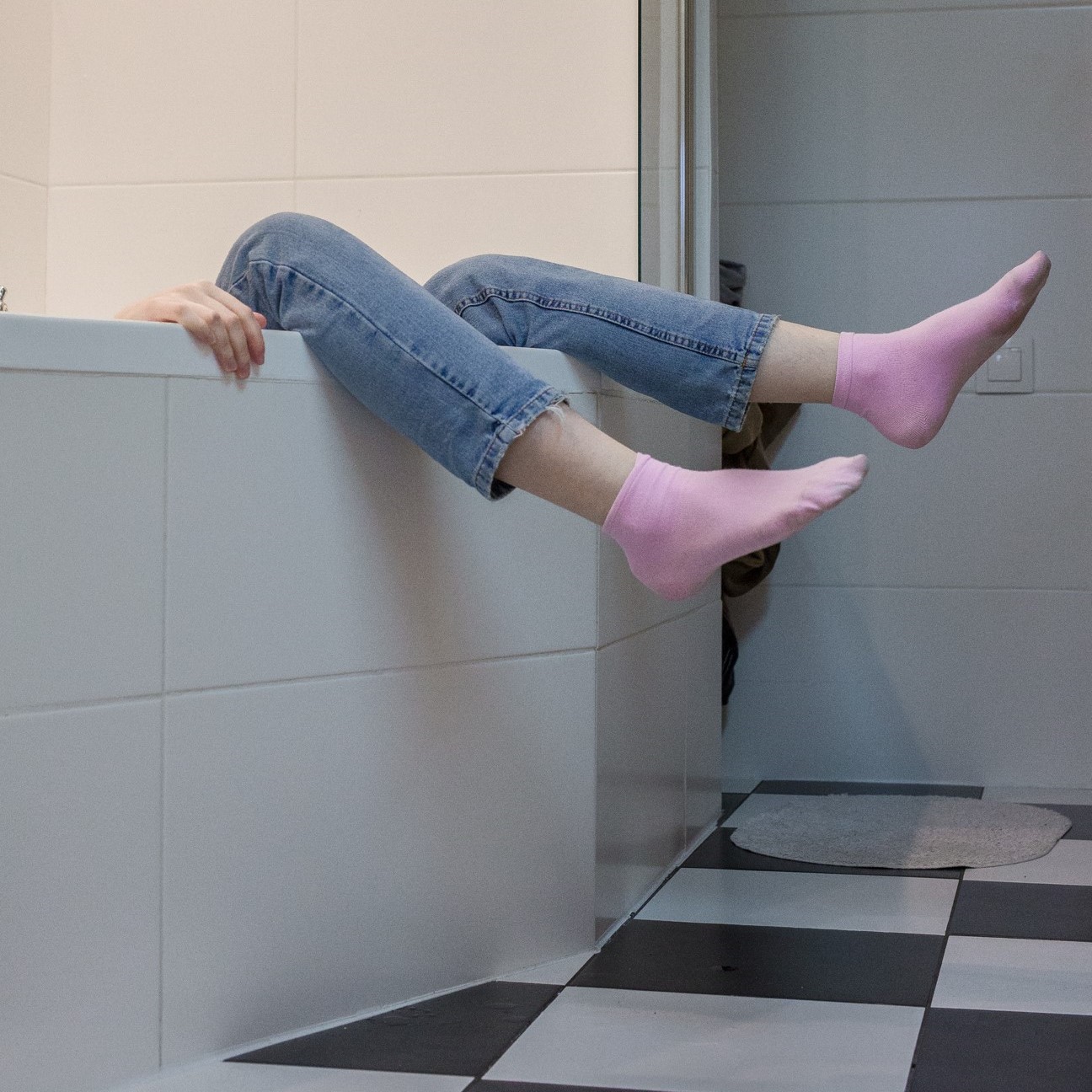 The legs with pink socks are sticking out of the bathtub.