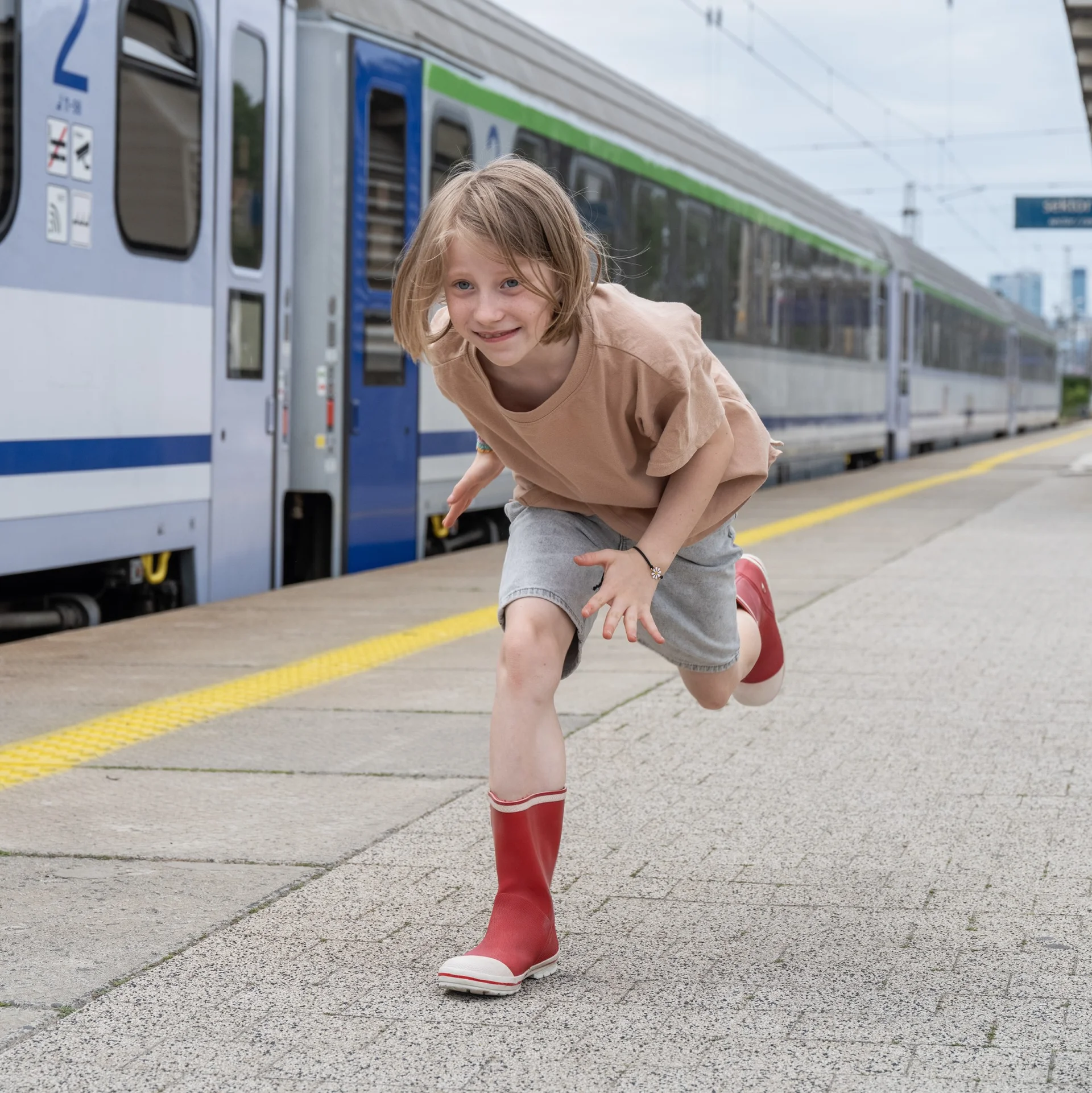 Dziewczynka w czerwonych kaloszach biegnie po peronie.