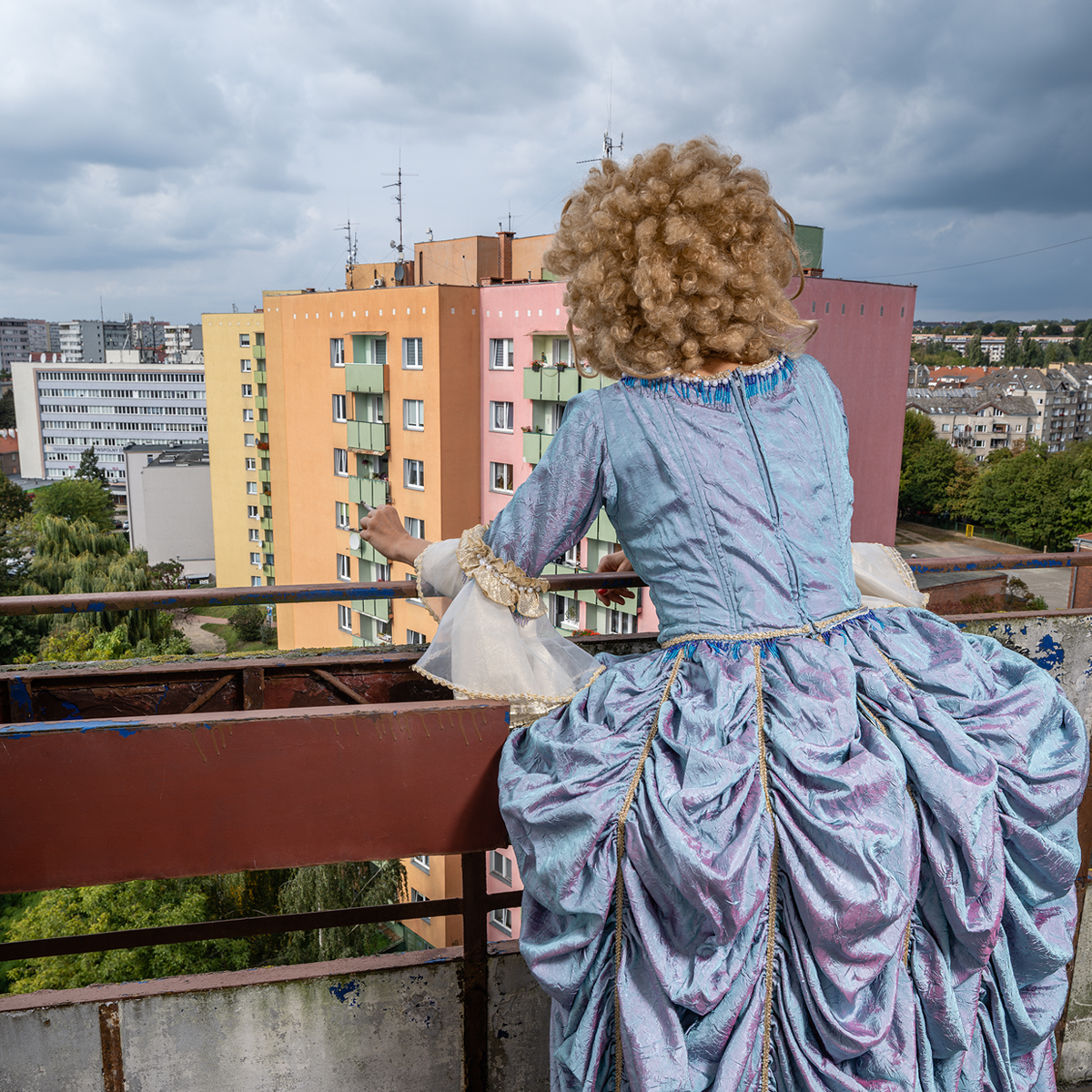 Kobieta w barokowej sukni stoi na balonie i patrzy na pastelowe bloki.