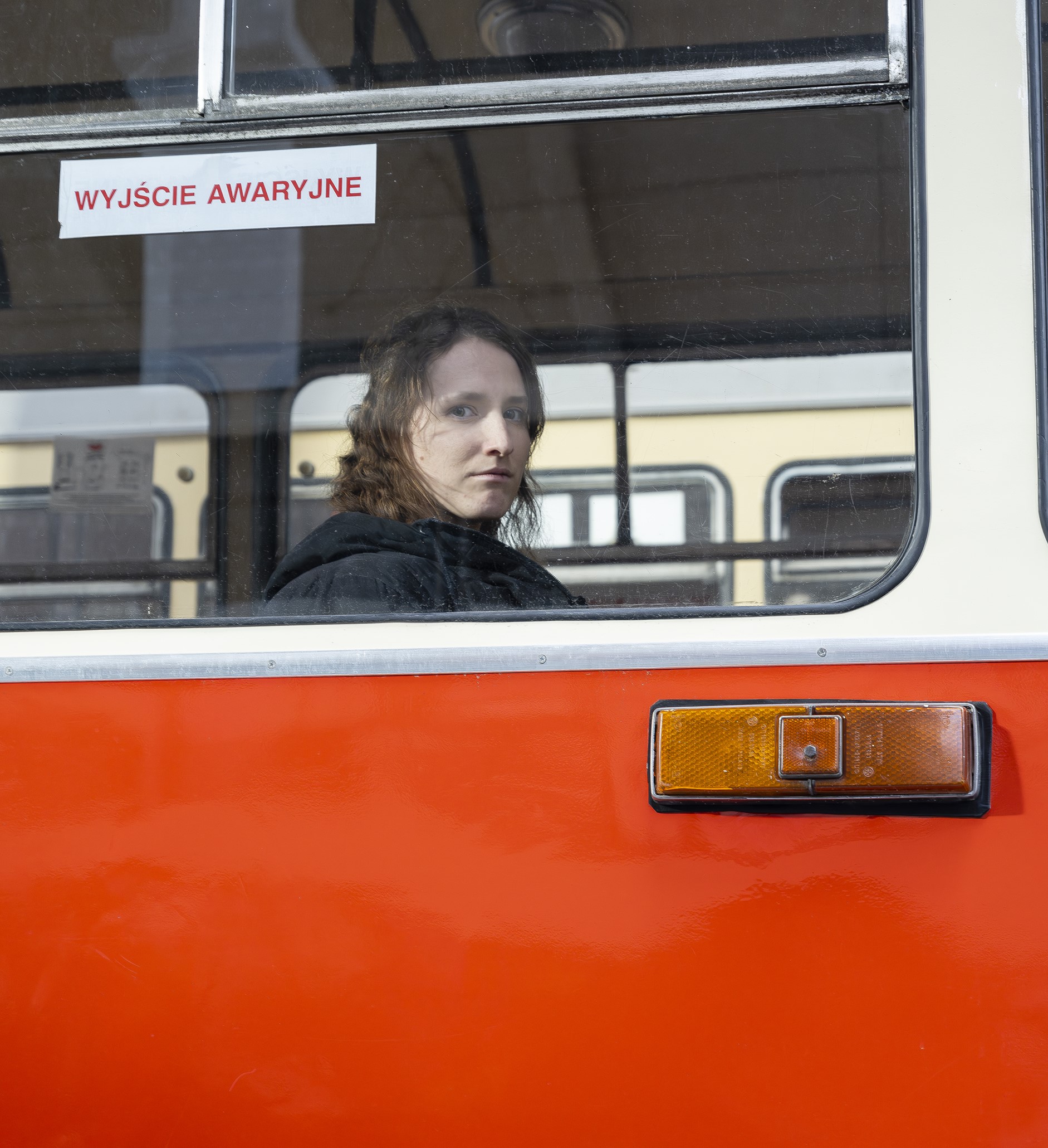 Młoda dziewczyna w czarnym ubraniu siedzi w czerwonym autobusie, smutno patrzy przez szybę.