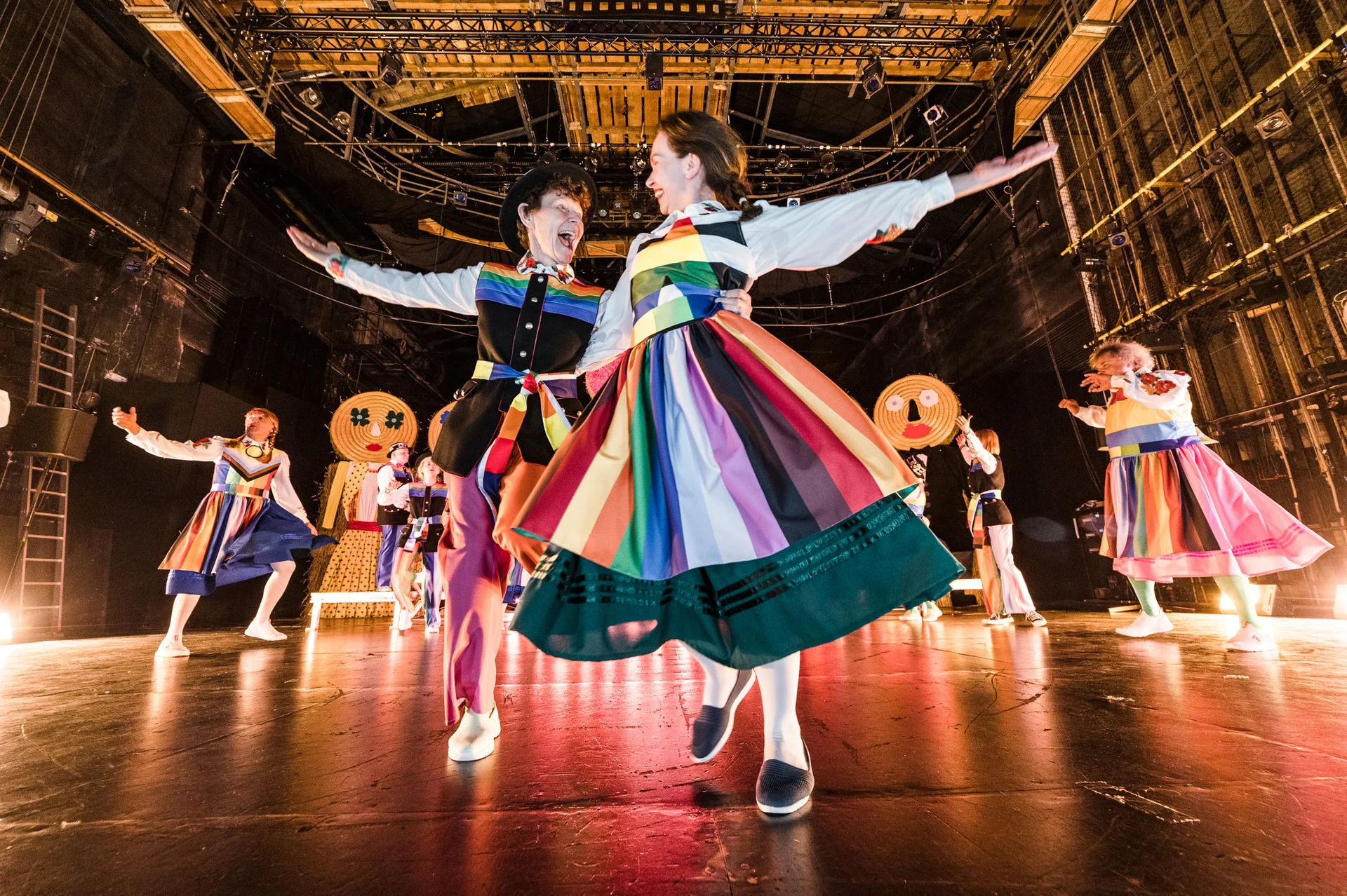 Dwie kobiety tańczą w strojach inspirowanych folklorem i flagami LGBTQ+.