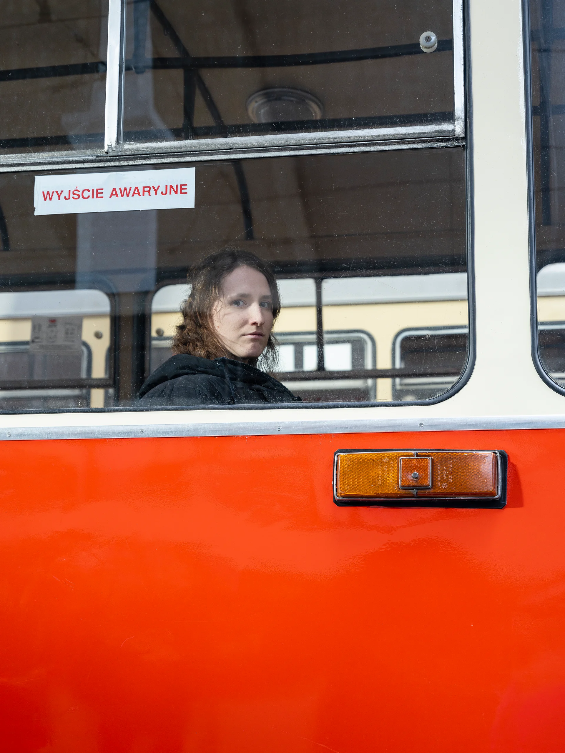 Młoda kobieta siedzi wewnątrz czerwonego autobusu. Smutnie patrzy w szybę. 