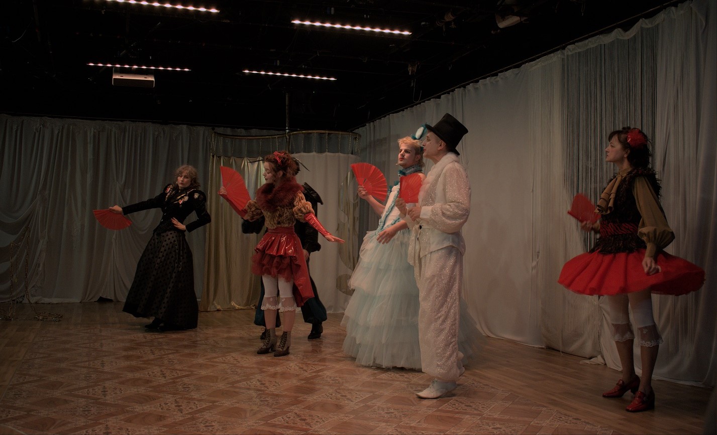 Zdjęcie ze spektaklu "XD dramma per musica". Kilkoro aktorów w strojnych kostiumach z czerwonymi wachlarzami w dłoniach.