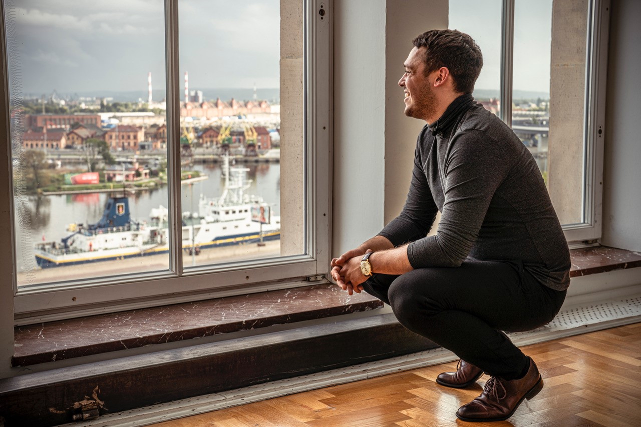 Jakub Skrzywanek pozujący na tle Odry w Małym Foyer teatru.