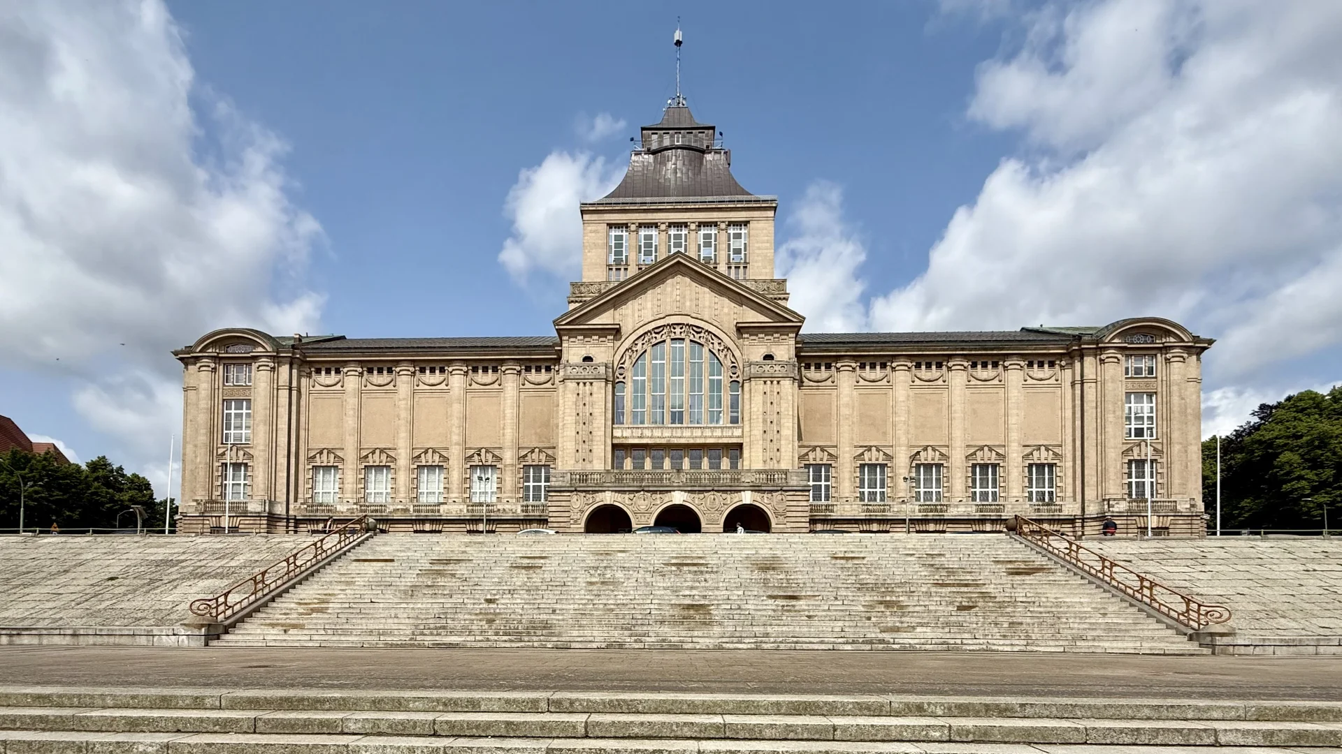 Zdjęcie Wałów Chrobrego. Budynek teatru i Muzeum Narodowego w całej okazałości. Przed nim schody. Po bokach widoczne drzewa. nad budynkiem jasne, lekko zachmurzone niebo. Budynek jest jasny, z wieżyczką w środkowej części.