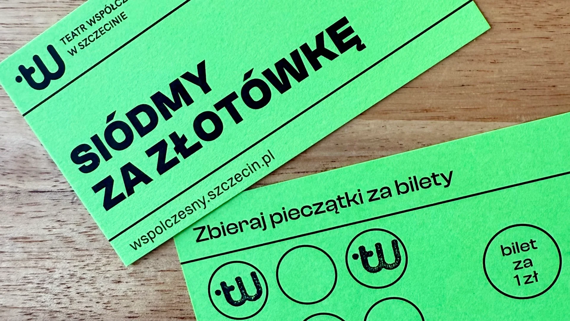 zdjęcie dwóch kart rabatowych leżących na stole. Jest to przód i tył tej samej karty w kolorze zielonym. Na przedniej stronie logo teatru i adres strony www, a także napis siódmy za złotówkę. Na drugiej karcie napis zbieraj pieczątki za bilety i siedem kółek. W niektórych z nich odbita jest pieczątka teatru. 