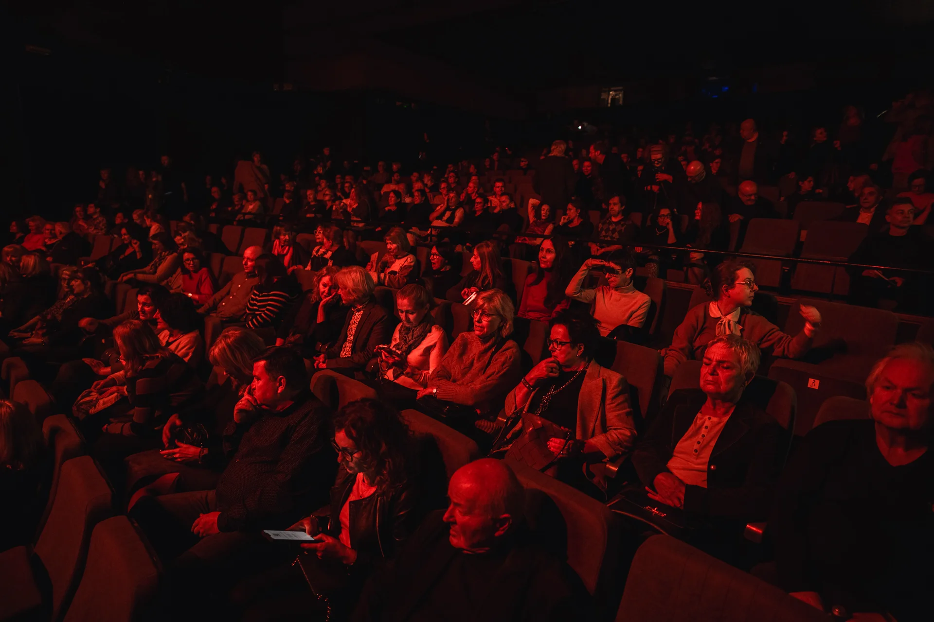 Zdjęcie pełnej teatralnej widowni, która jest podświetlona na czerwono.
