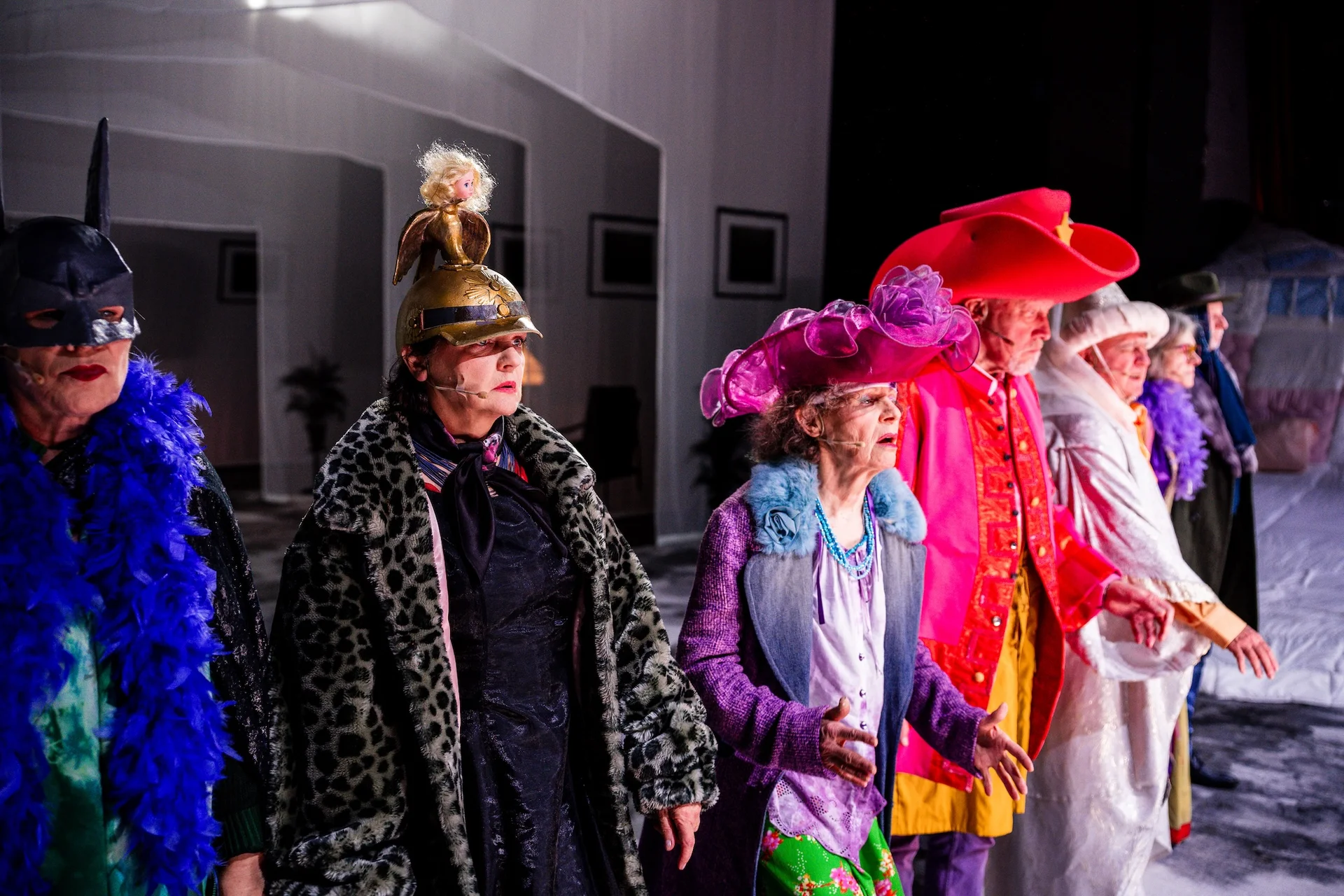 fot. Piotr Nykowski Grupa starszych aktorów w śmiesznych przebraniach stoi na scenie. Inscenizują nieudany teatrzyk. Wszyscy mają dziwaczne nakrycia głowy - wielki czerwony kapelusz, maskę Batmana czy hełm starożytnego żołnierza.