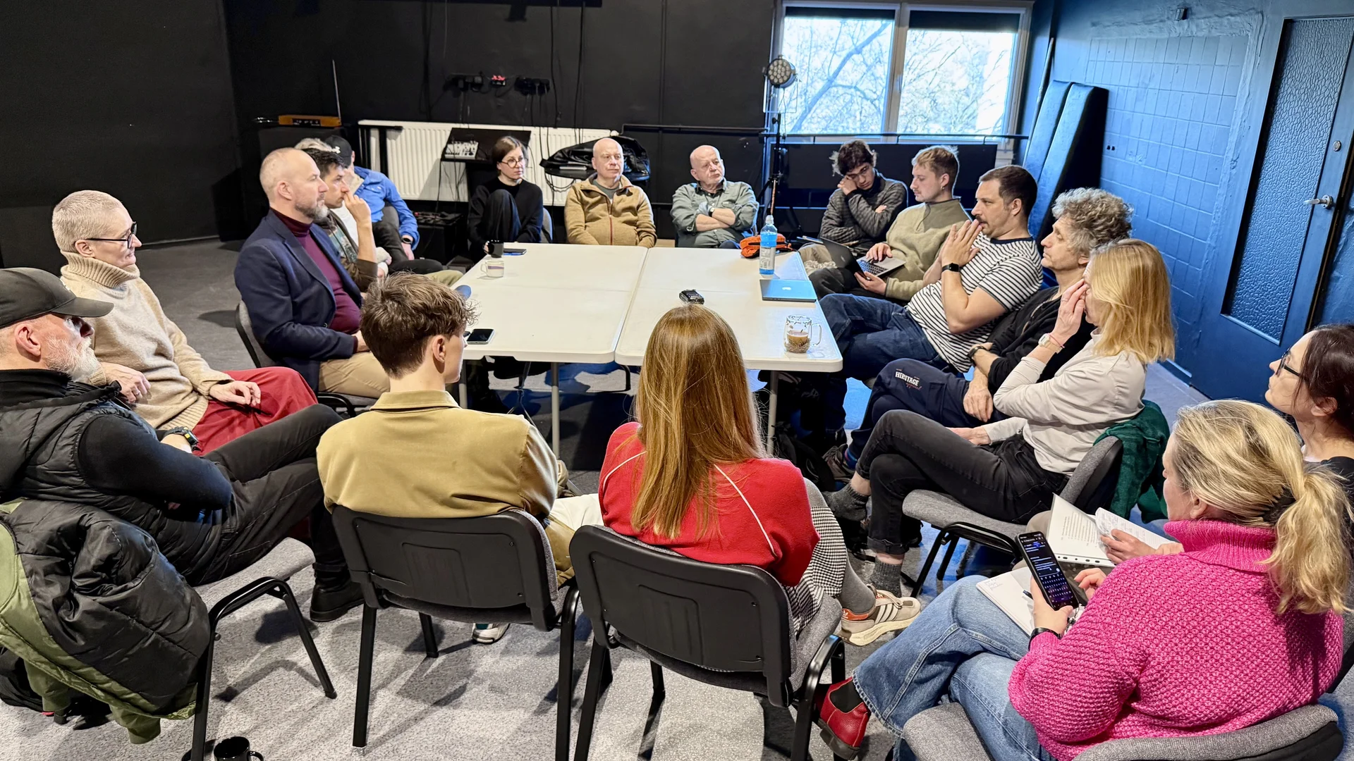 Zdjęcie z salki prób. Pierwsza próba do spektaklu SZTUKA PROTESTU - grupa aktorów i realizatorów siedzi na krzesłach dookoła białego stołu.