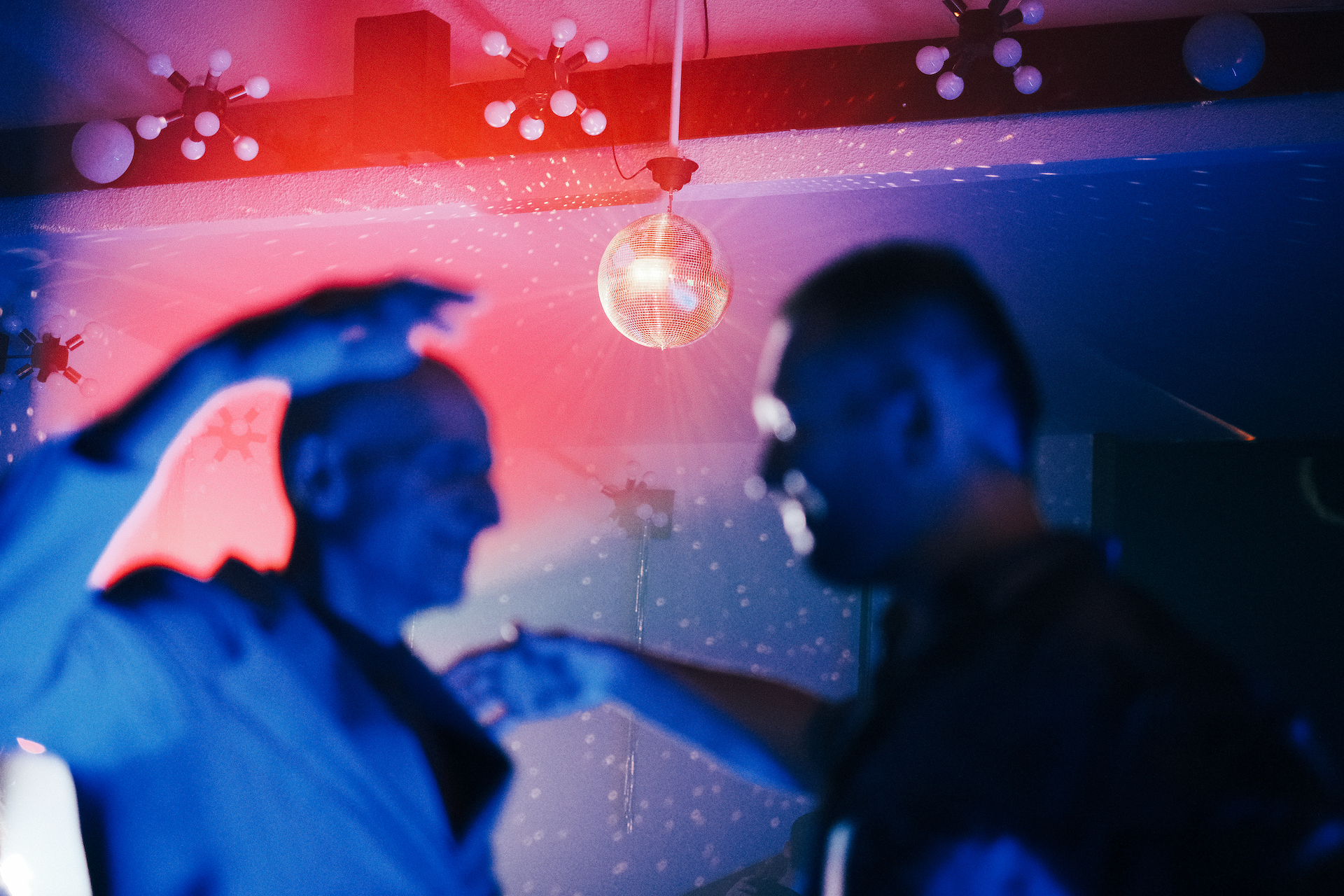 Zdjęcie ze spektaklu Dotyk za dotyk. dansing. Kolorowe światła i kula dyskotekowa. Dwóch mężczyzn tańczy razem. 