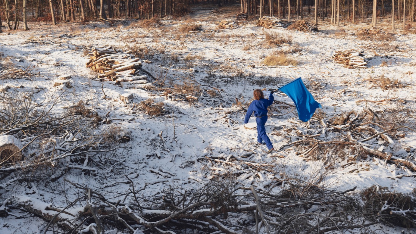 fot. Mila Łapko Młody mężczyzna w niebieskim kombinezonie i z niebieską flagą biegnie przez miejsce wycinki lasu.