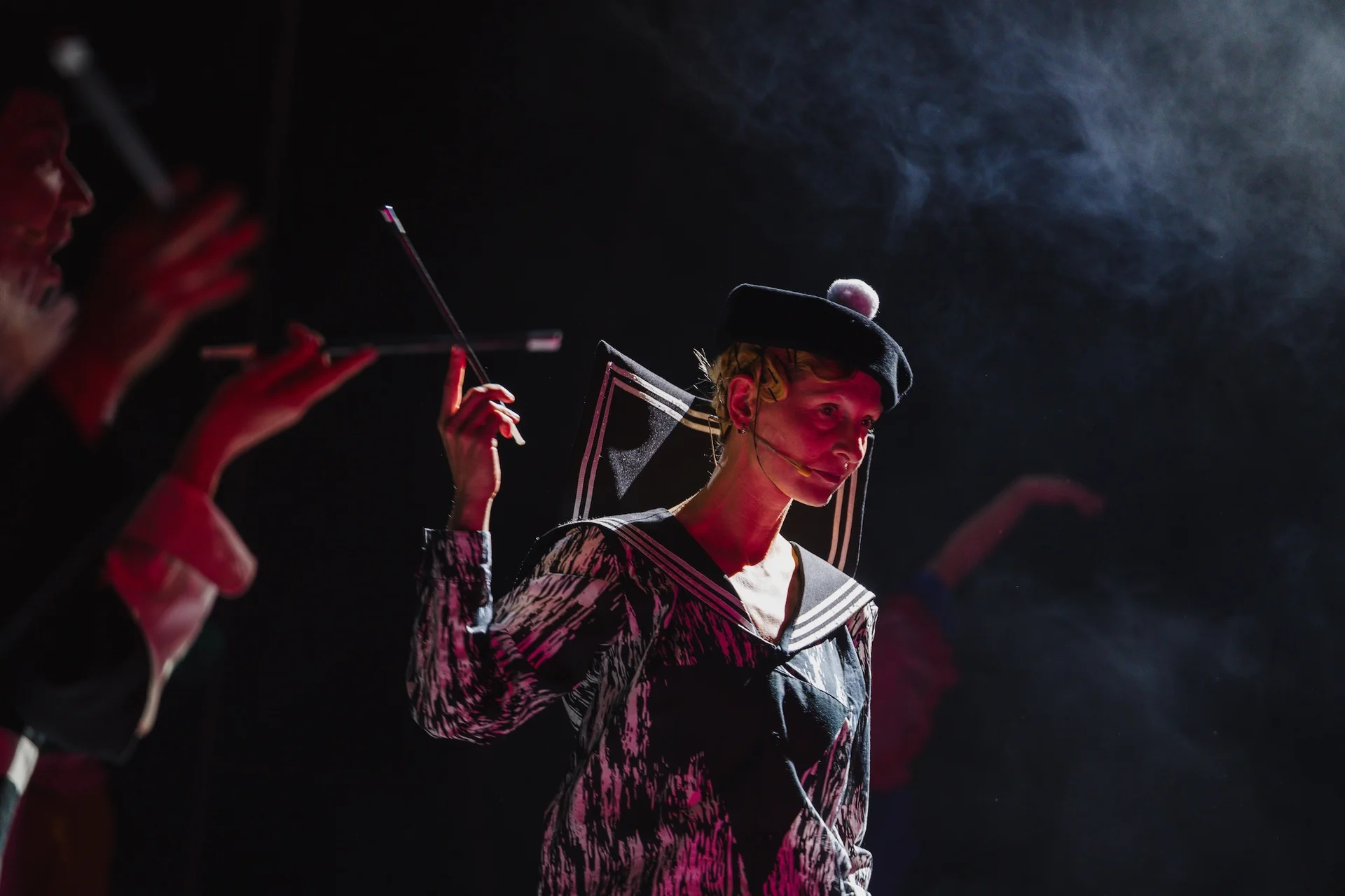 Kobieta ubrana w czarno-biały strój stoi w półmroku. Nad nią unosi się dym. Unosi lewą rękę, w której trzyma cygaretkę. Na głowie ma ubrany czarny beret z białym pomponem.