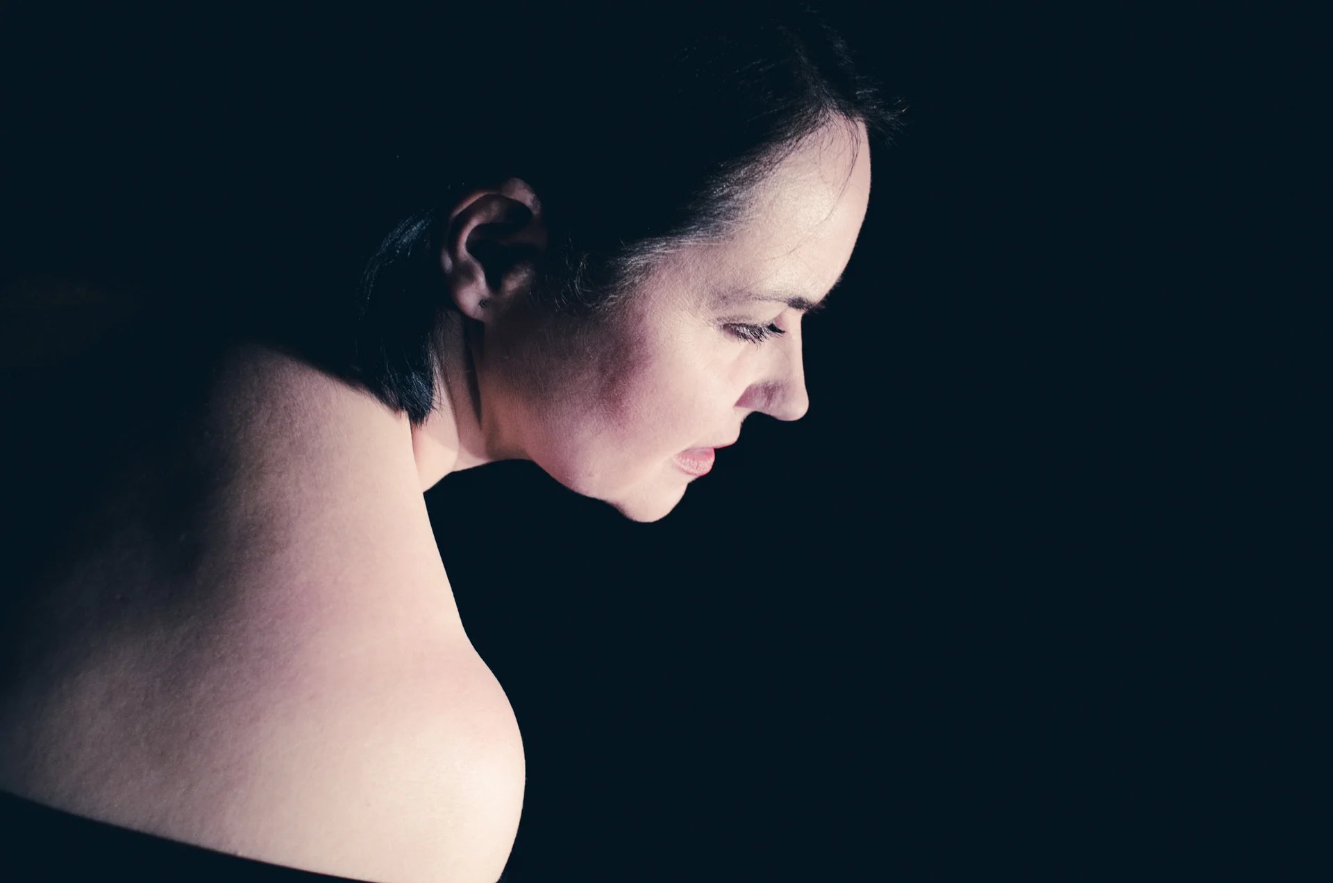 fot. Piotr Nykowski Profil i odsłonięte ramię aktorki. Czarne tło.