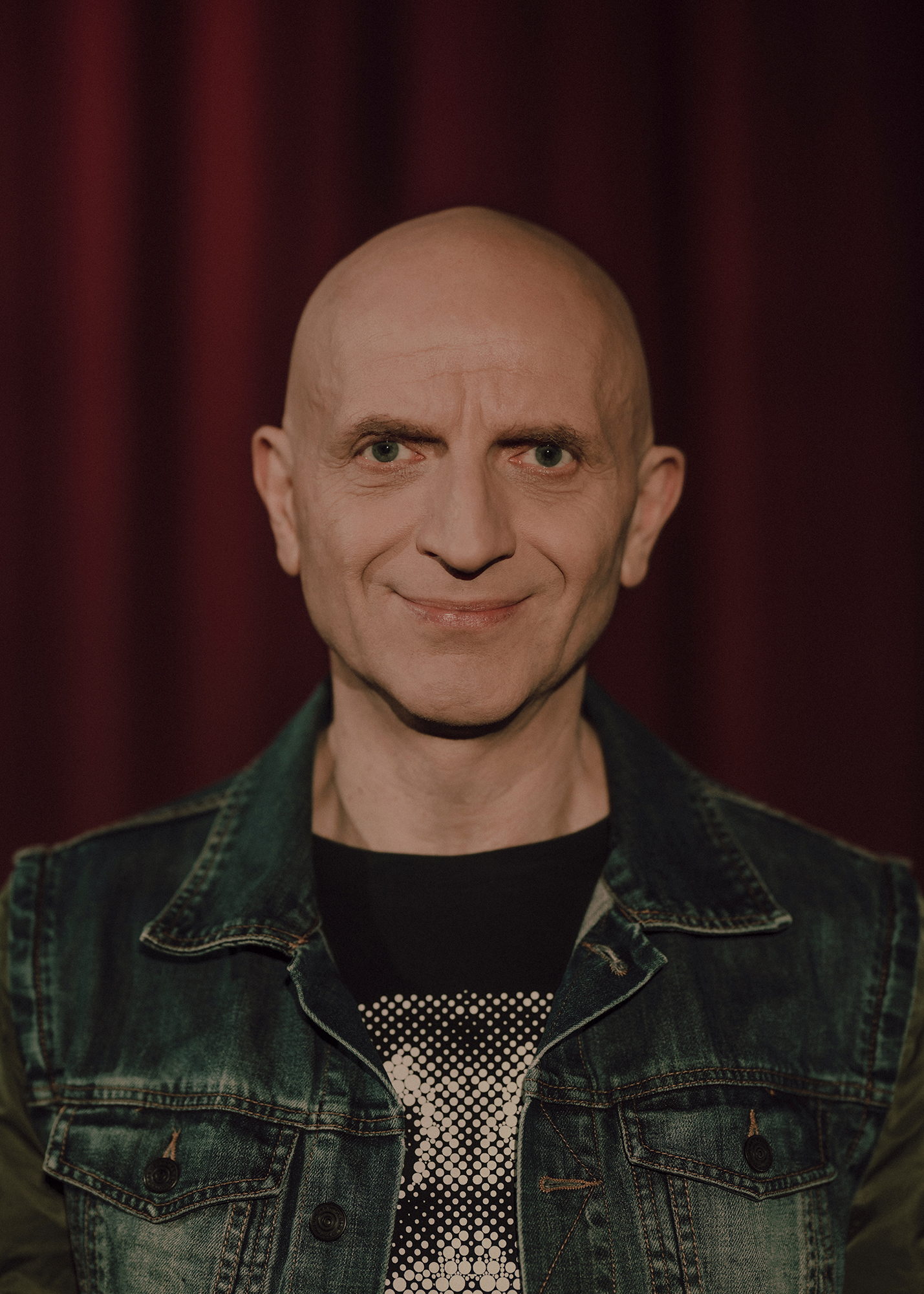 Portret aktora na tle czerwonej kotary.