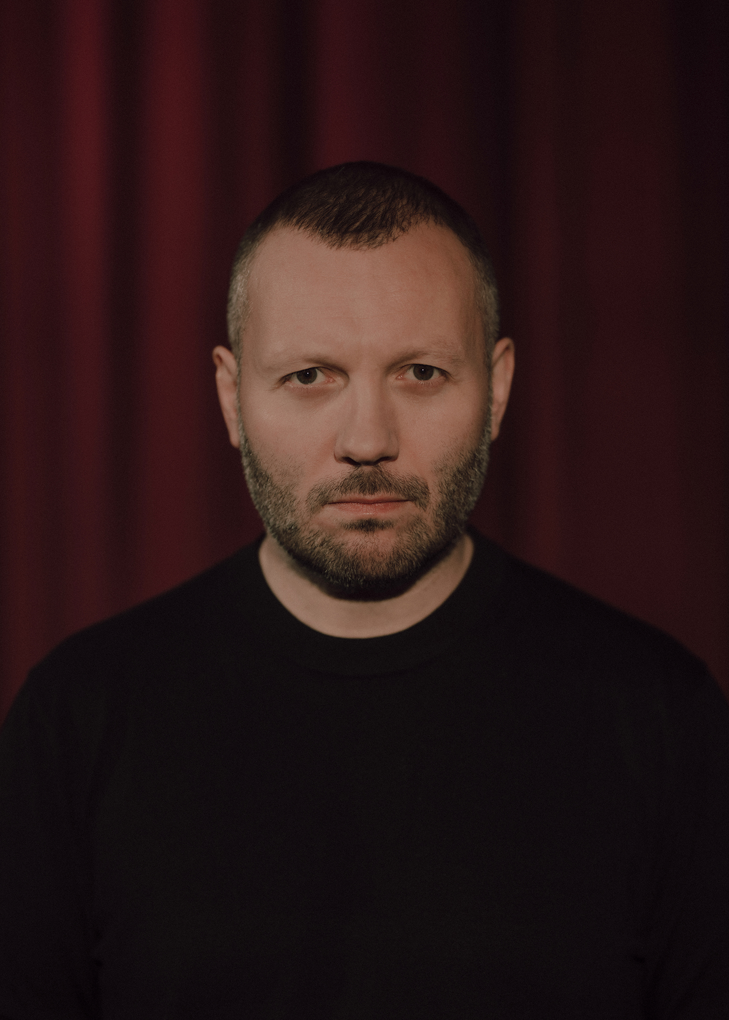 Portret aktora, w tle czerwona kotara.