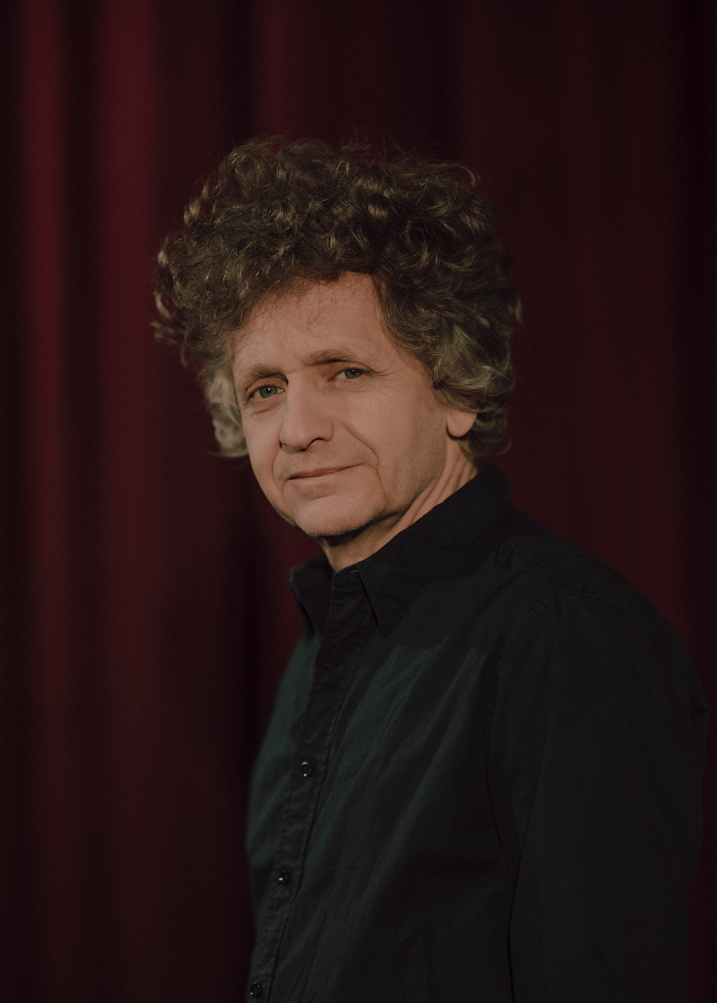 Portret aktora, w tle czerwona kotara.