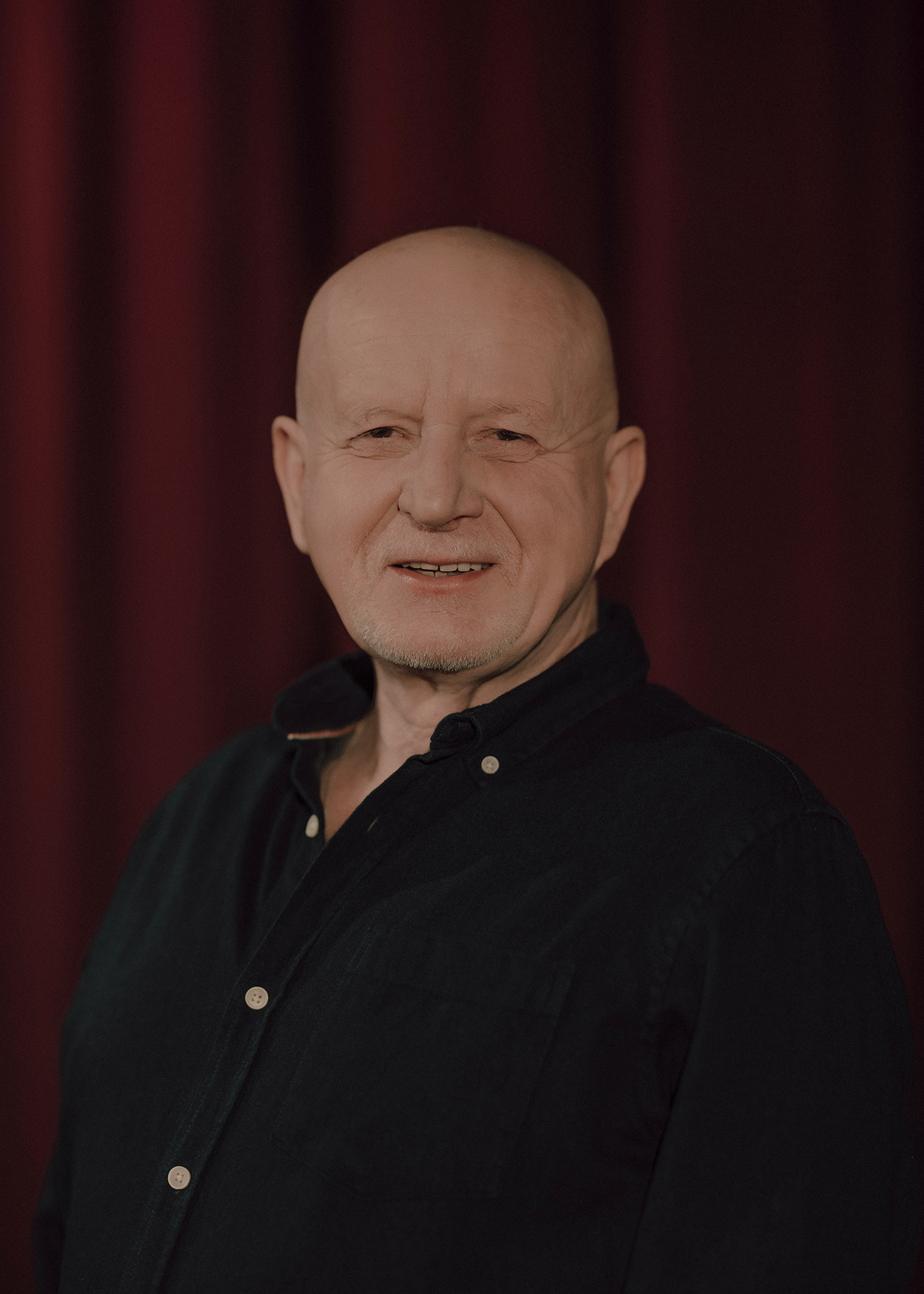 Portret aktora, w tle czerwona kotara.