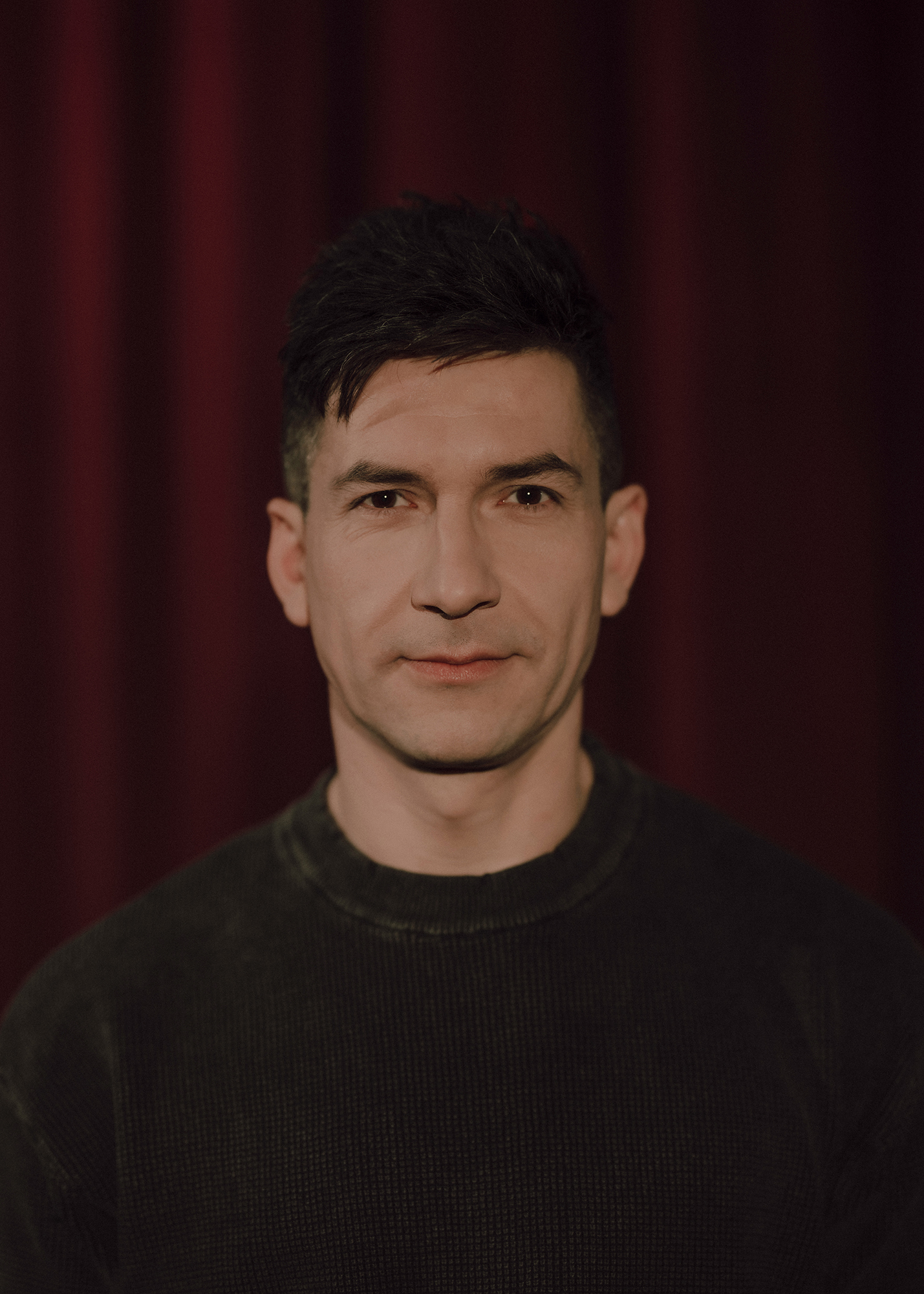 Portret aktora, w tle czerwona kotara.