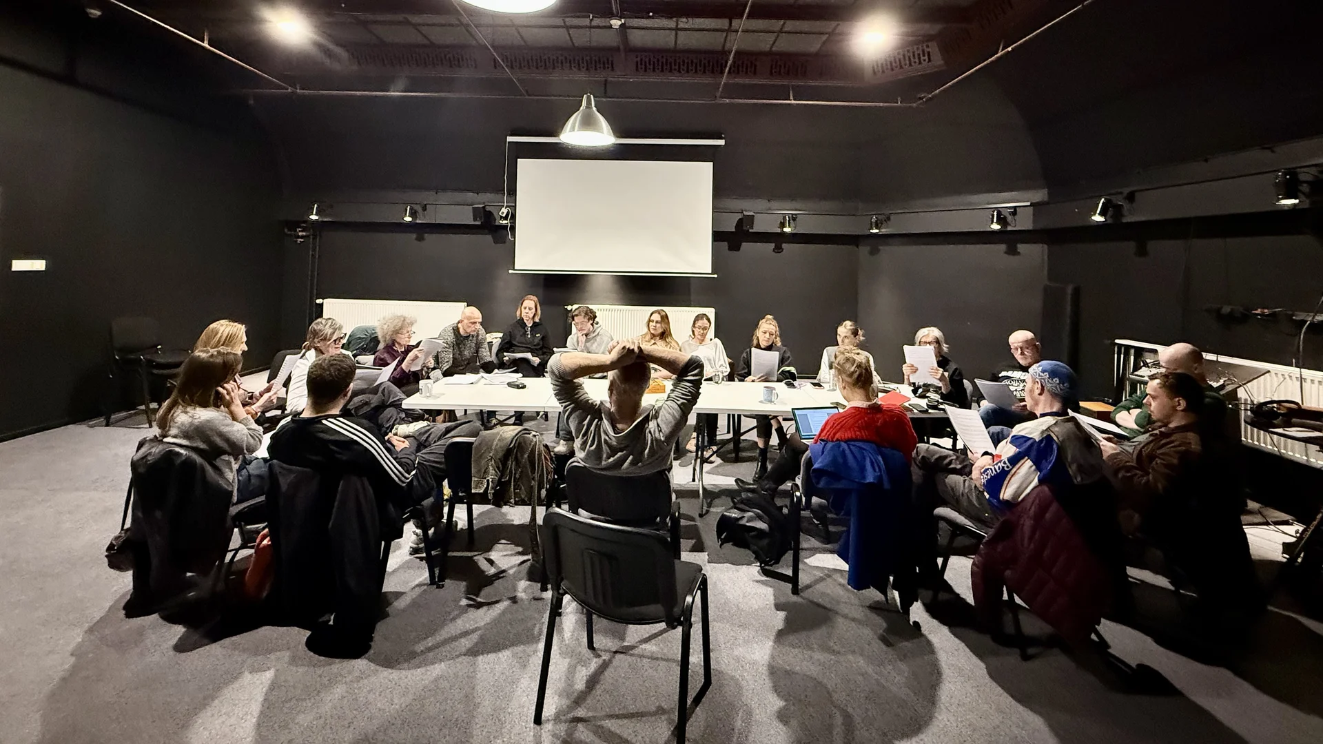 Zdjęcie z salki prób. Grupa aktorów przy siedzi przy stole. Odbywa się pierwsze czytanie scenariusza. 