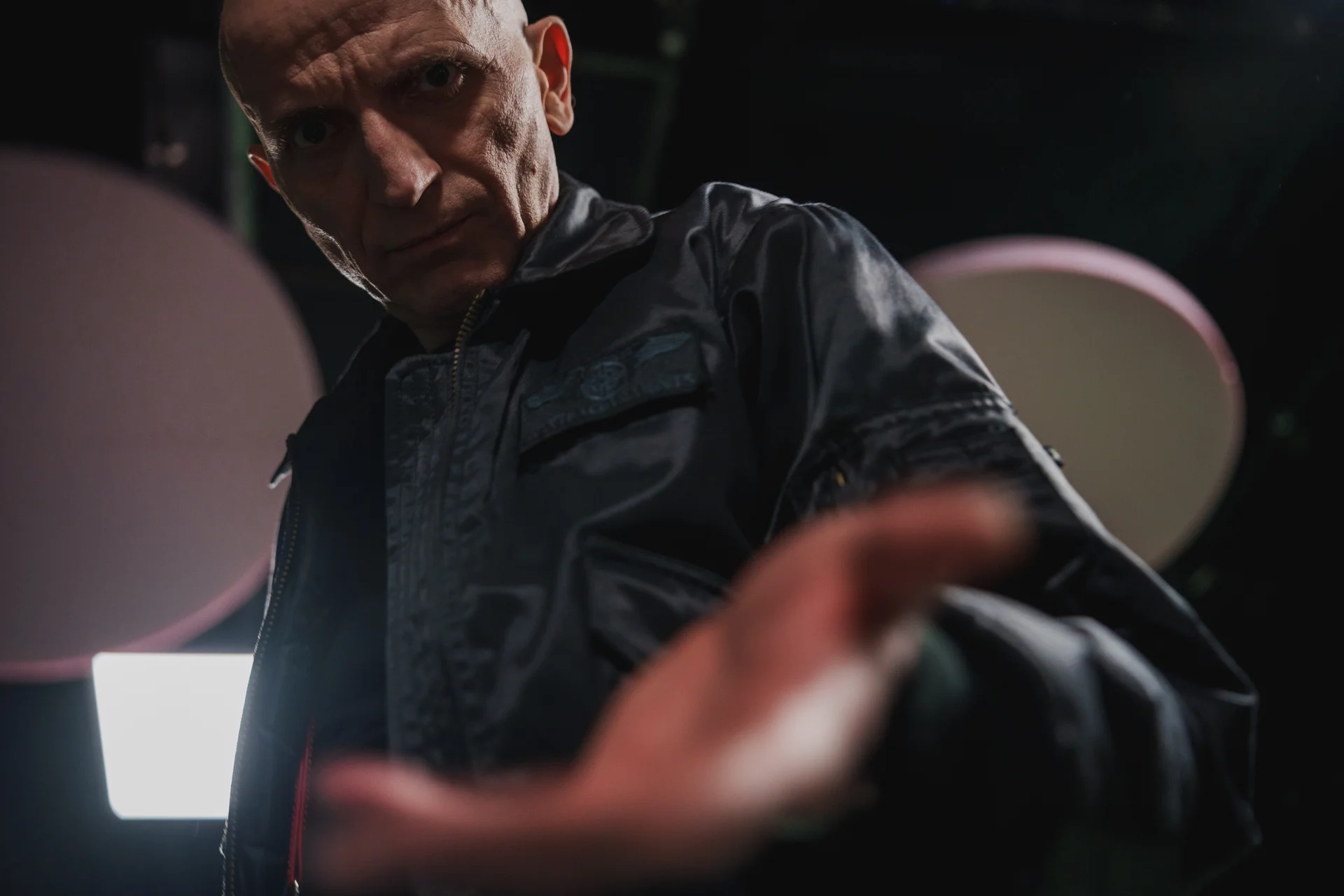 „Piękny i krótki spektakl o komunikacji”, fot. Piotr Nykowski Aktor w czarnej kurtce wyciąga dłoń w stronę aparatu.