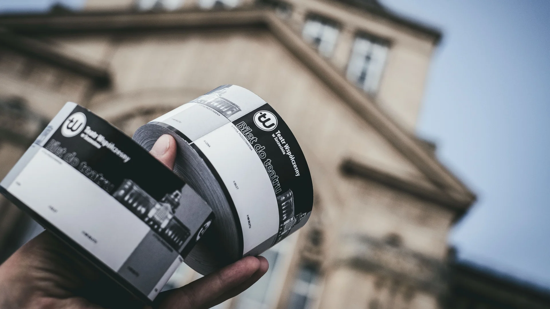 Zdjęcie rolek biletów w dłoni. Trzymane na tle budynku teatru. 