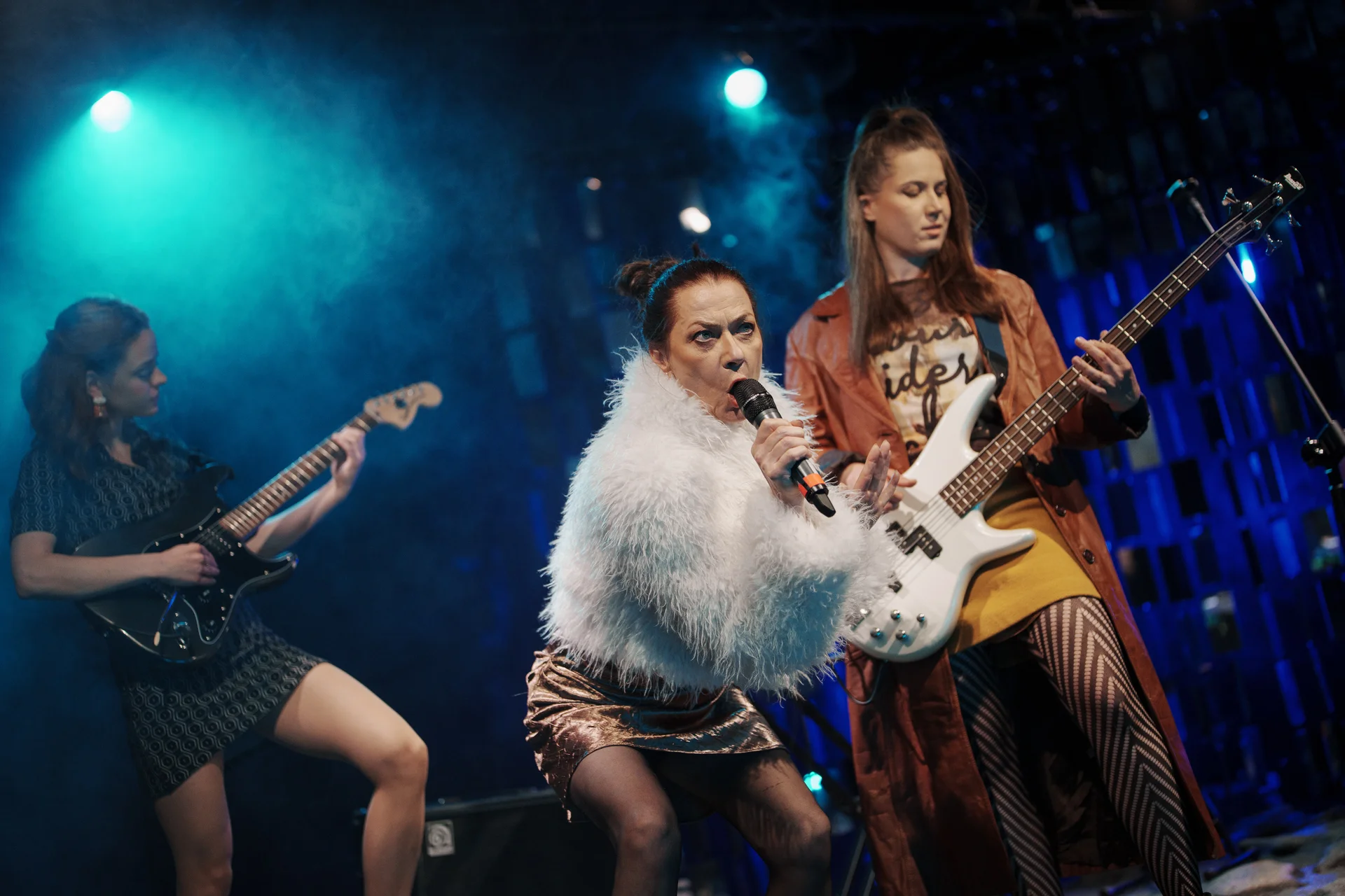 Trzy kobiety stojące na ruinach. Pierwsza ubrana w krótką sukienkę w srebrnych szpilkach. Stoi jedną nogą na kamieniu przy głośnikach. Trzyma gitarę elektryczną. Druga kobieta ubrana w białe futro oraz krótką sukienkę. Tańcząca na boso z mikrofonem w dłoni. Trzecia w długim płaszczu i rajstopach. Skupiona na graniu na gitarze elektrycznej.
