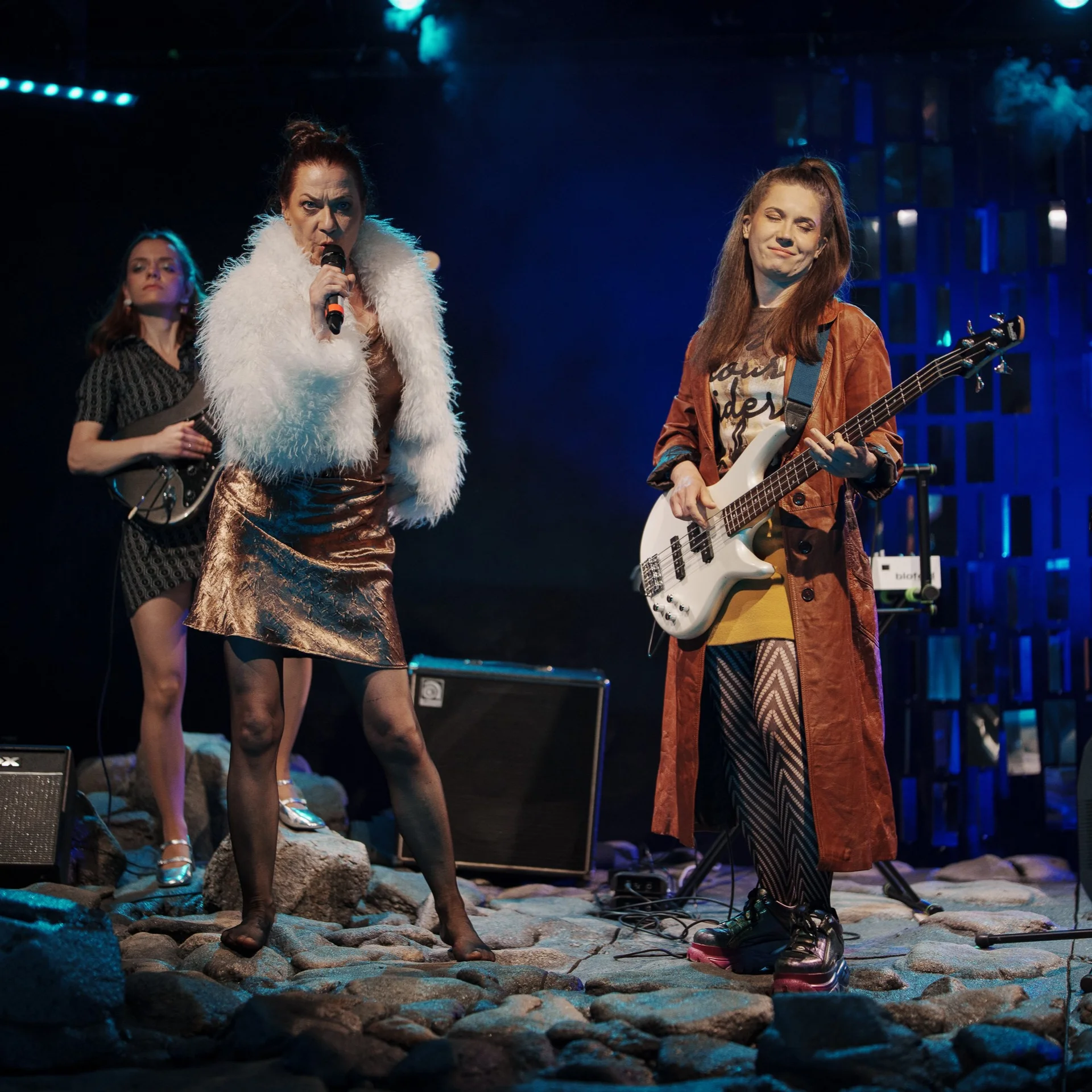 fot. Piotr Nykowski Trzy aktorki występujące na scenie. Po prawej stronie kobieta w długim brązowym płaszczu gra na gitarze basowej. Obok niej aktorka w krótkim białym futrze trzyma mikrofon. W tle trzecia kobieta w krótkiej szarej sukience gra na gitarze.
