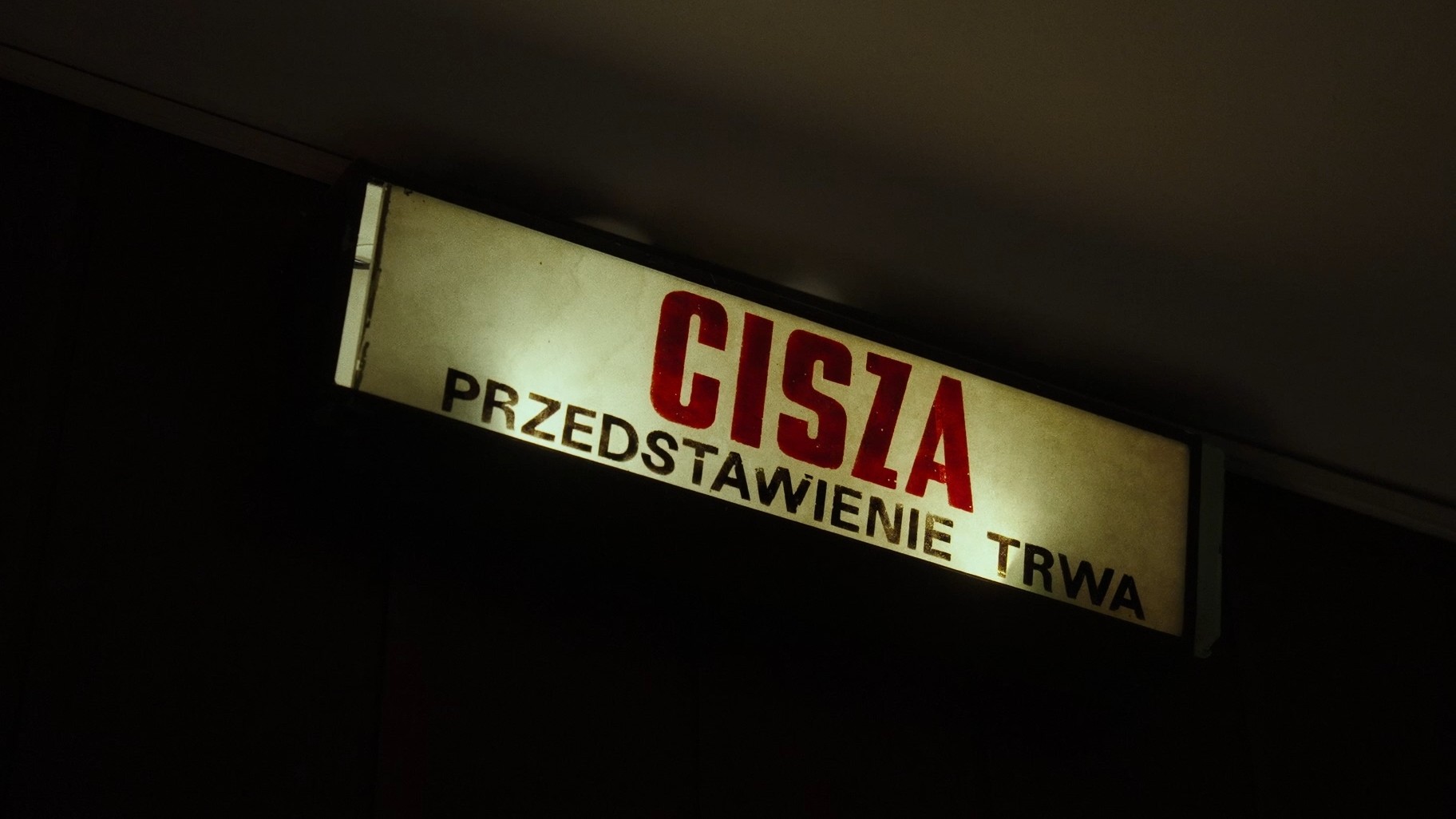 Kadr z filmu Kadr z filmu. Na czarnym tle zapalona lampa z napisem: Cisza. Przedstawienie trwa.