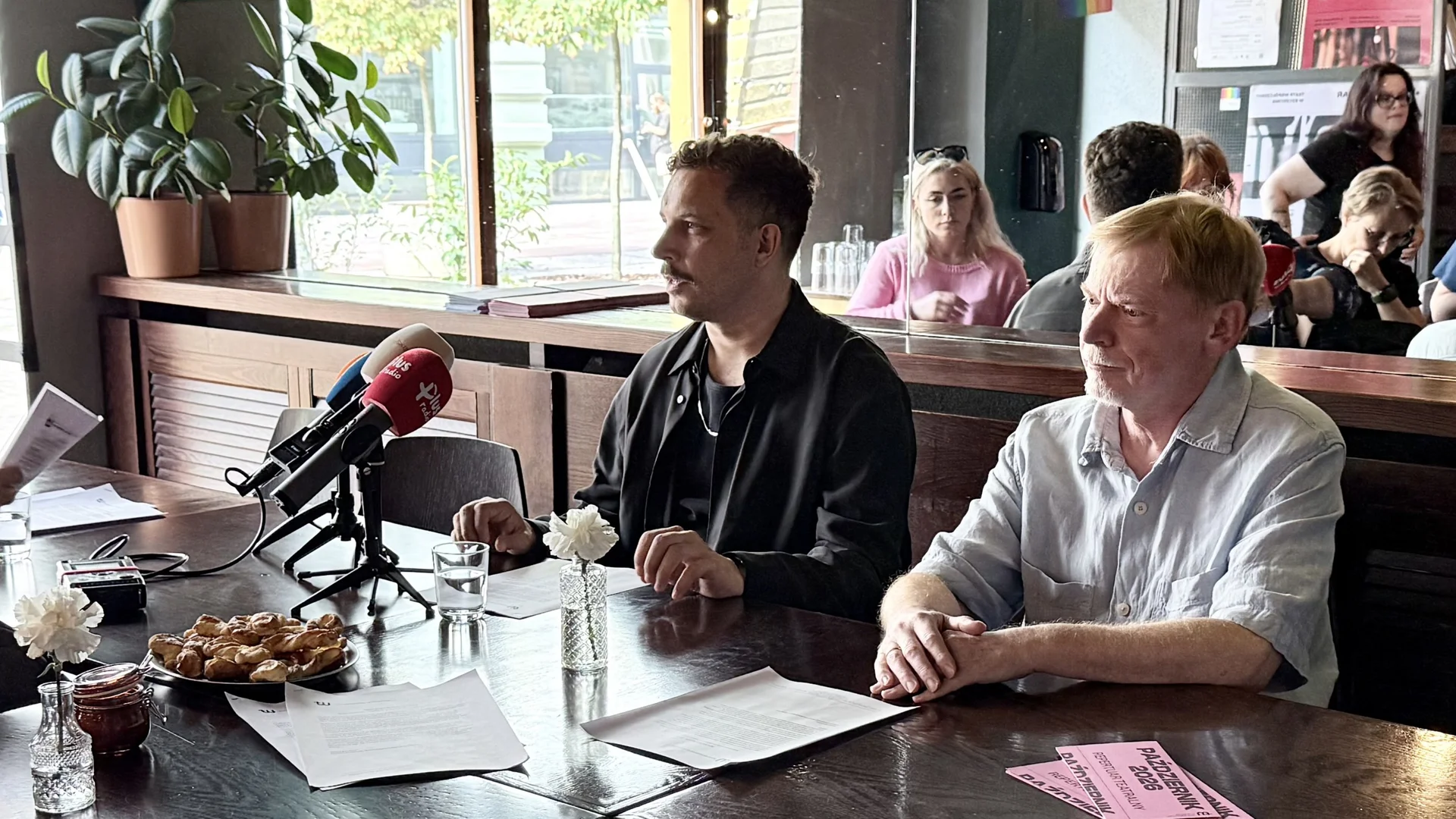 zdjęcie z konferencji sezonowej w Teatrze Małym - na zdjęciu dyrektorzy Michał Buszewicz i Mirosław Gawęda. Obaj siedzą przy stole. przed nimi kartki, wazoniki z kwiatami. Przed dyrektorem Buszewiczem stoją mikrofony radiowe